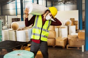 Male workers carry heavy rolls of fabric over their shoulders to move them into production and are at risk of injury from lifting too heavy loads