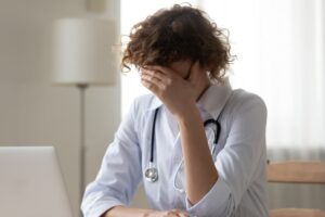 Unhappy stressed young woman doctor covering face with hand, upset worried due to death of a patient