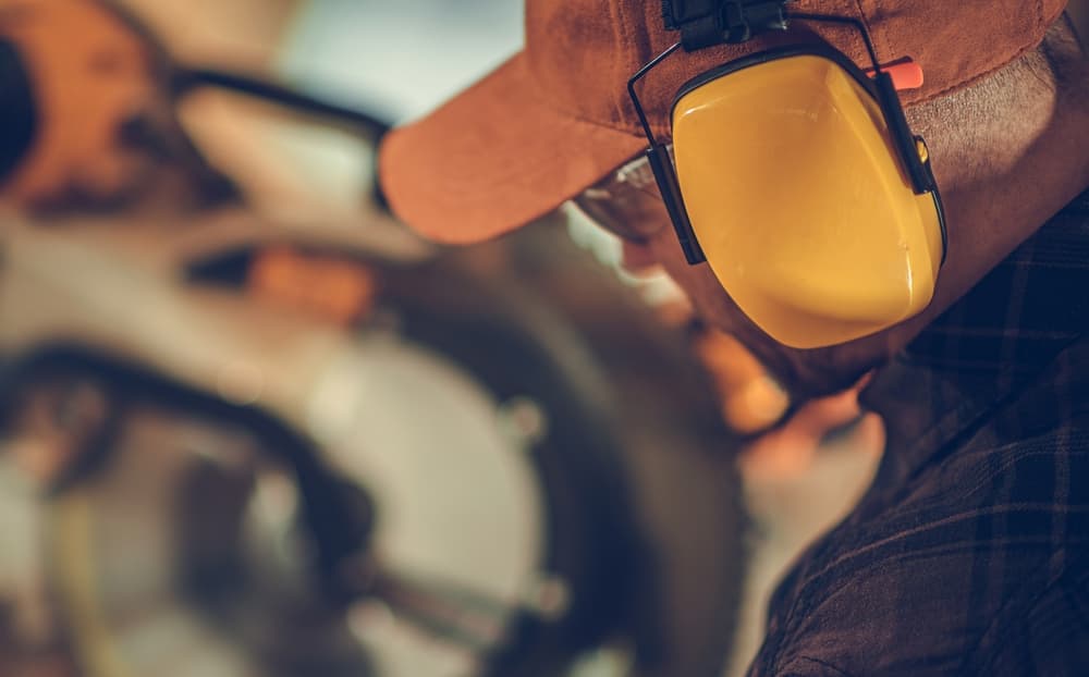 Caucasian Construction Worker in His 40s Wearing Noise Cancellation Safety Headphones While Working Within Construction Site.