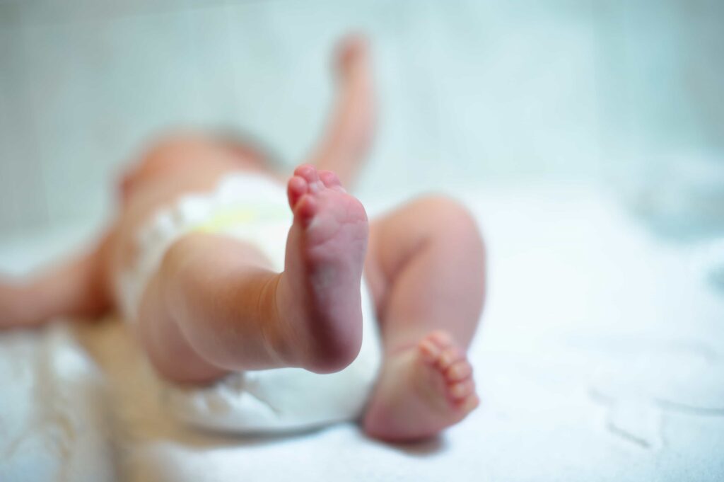 Newborn baby lying on bed in diaper with focus on tiny feet