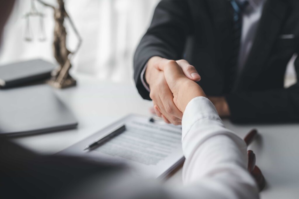 Lawyer and client shaking hands over legal documents in office Lawyer and client shaking hands over legal documents in office