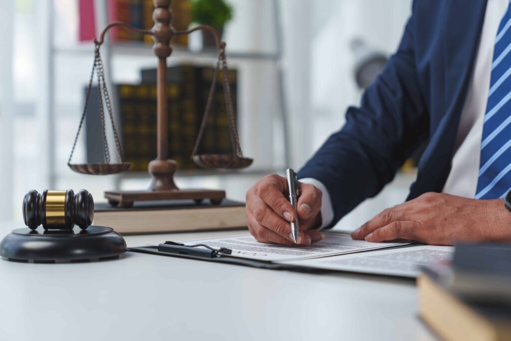 Lawyer signing legal documents with gavel and scales of justice on desk