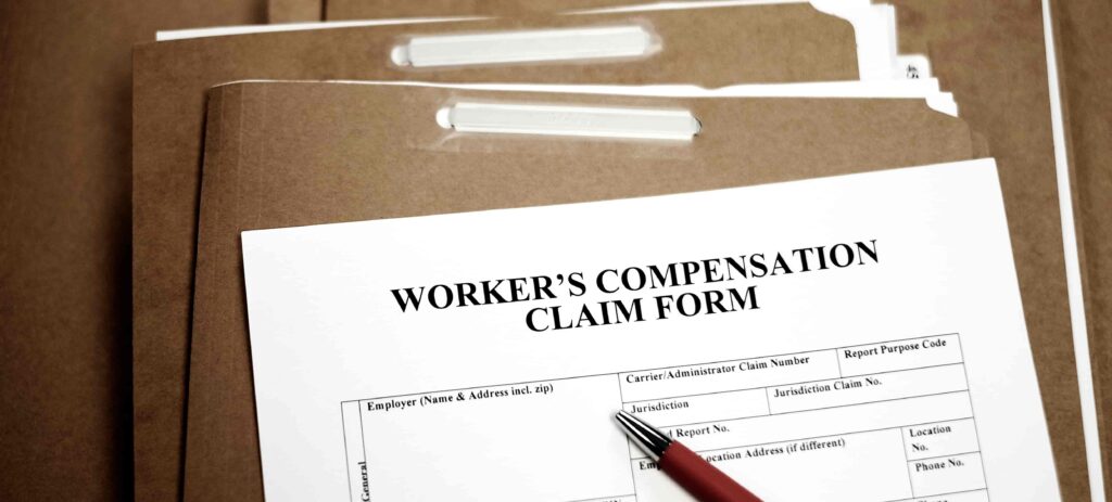 Worker’s compensation claim form with pen and file folders for workplace injury benefits application.
