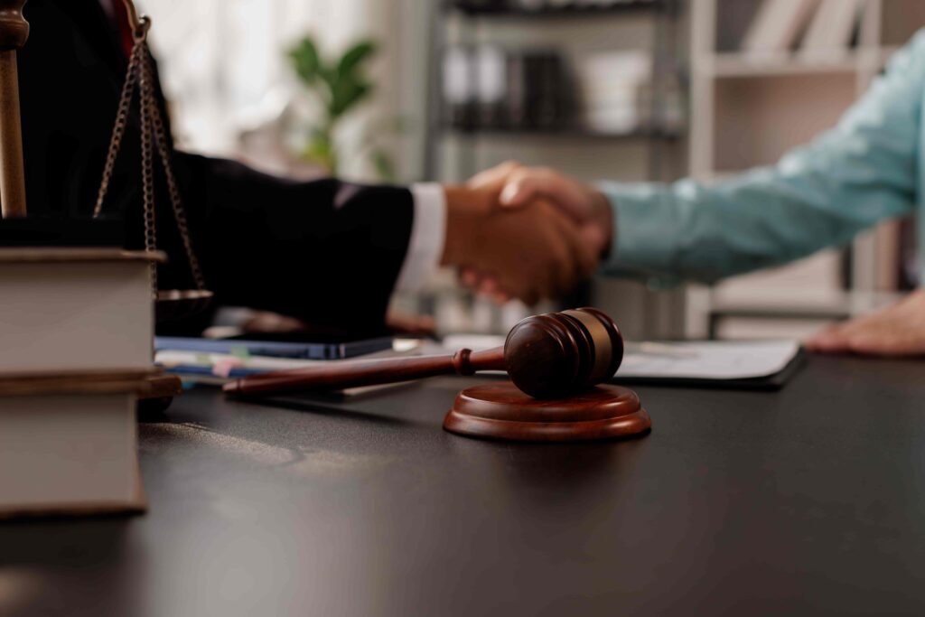Lawyer and client shaking hands in office with gavel and legal books on desk