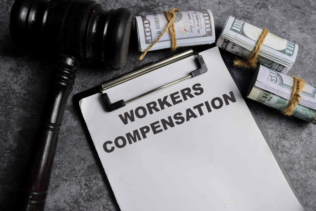 Workers’ compensation document with gavel and money rolls symbolizing legal claims and financial benefits for workplace injuries. Workers’ compensation document with gavel and money rolls symbolizing legal claims and financial benefits for workplace injuries.