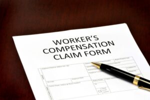 Worker’s compensation claim form with pen and file folders for workplace injury benefits application.